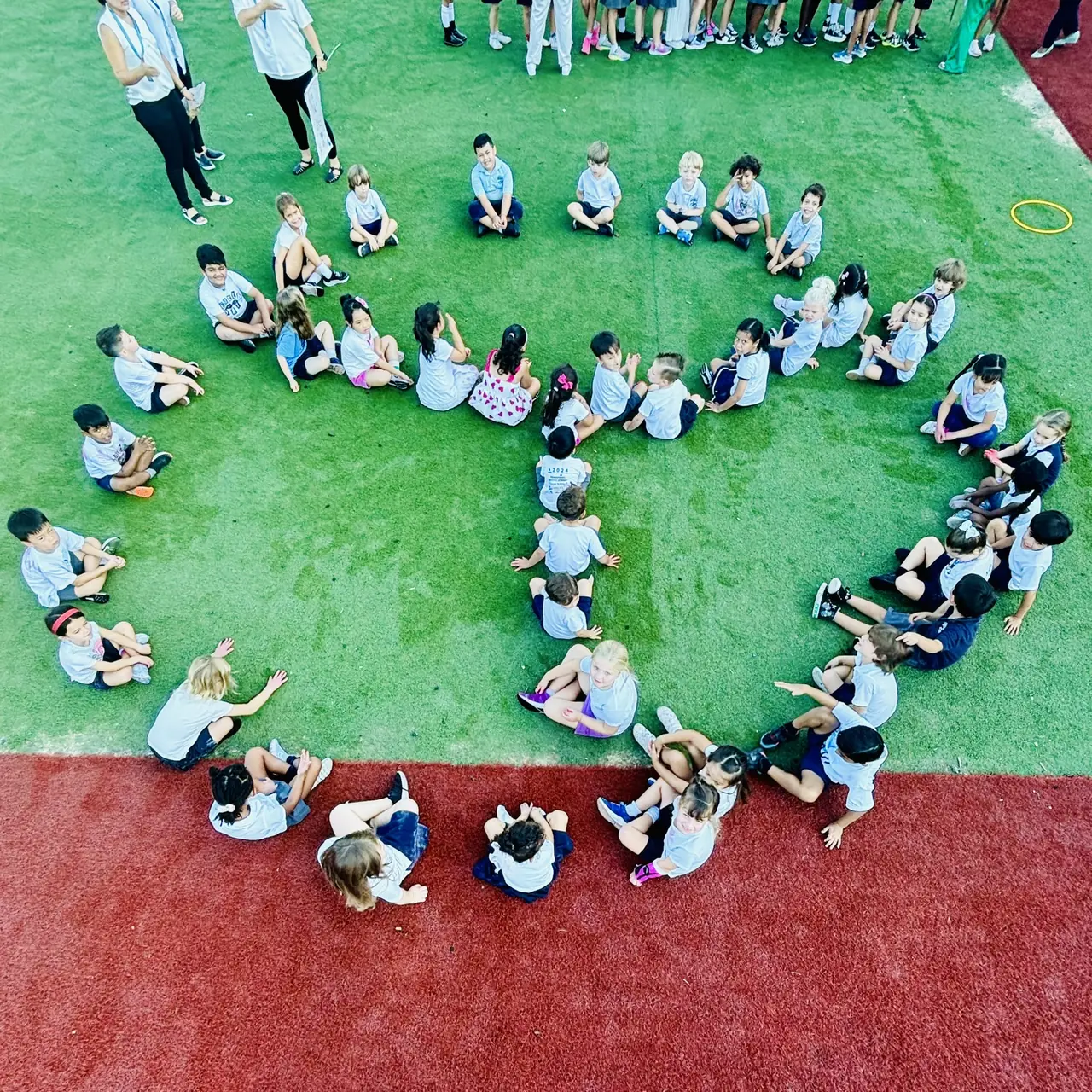 Students seated in a large circle on the field, seen from above